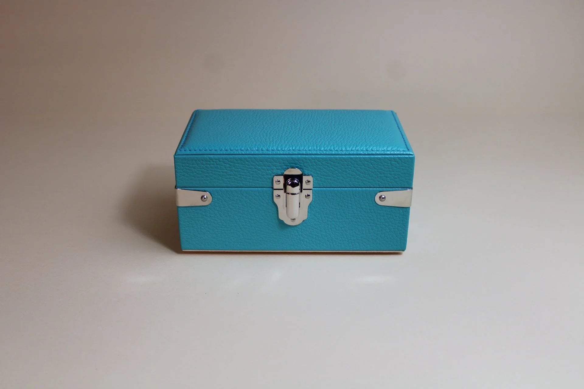 Blue textured leather box with silver clasp on neutral background