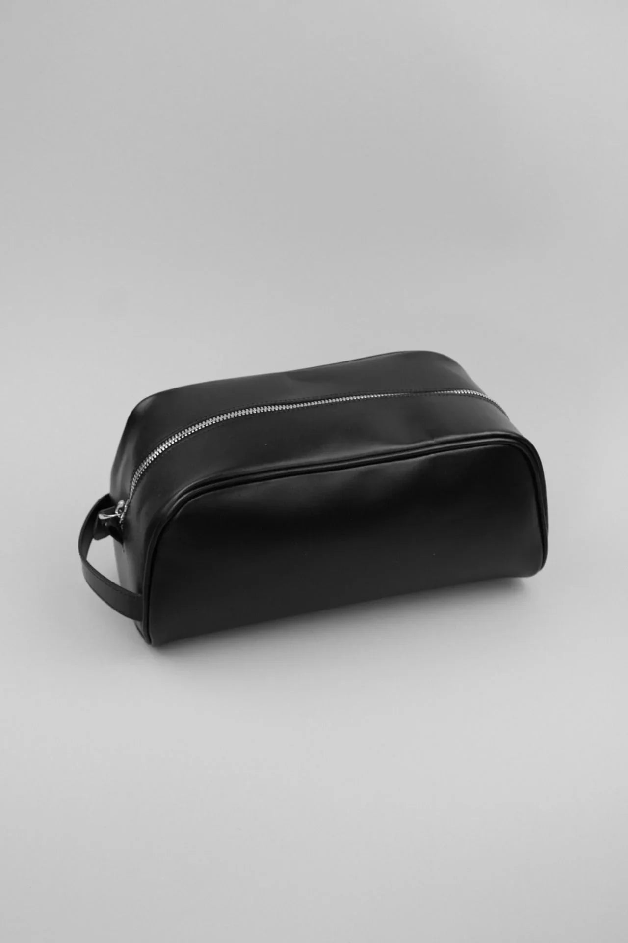 Black leather toiletry bag with zipper on plain background