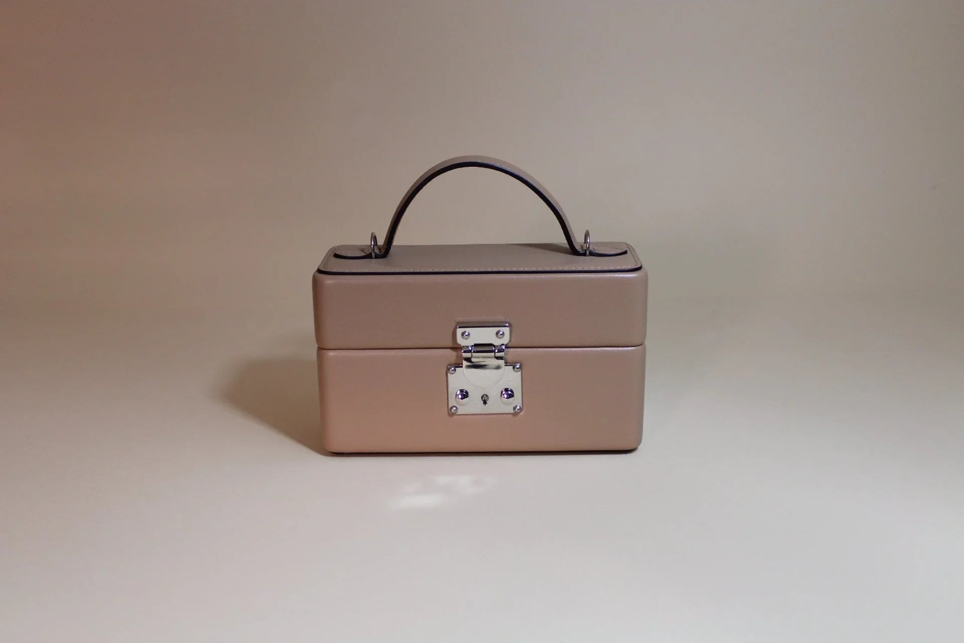 Beige leather box-shaped handbag with top handle and silver clasp, minimalist background