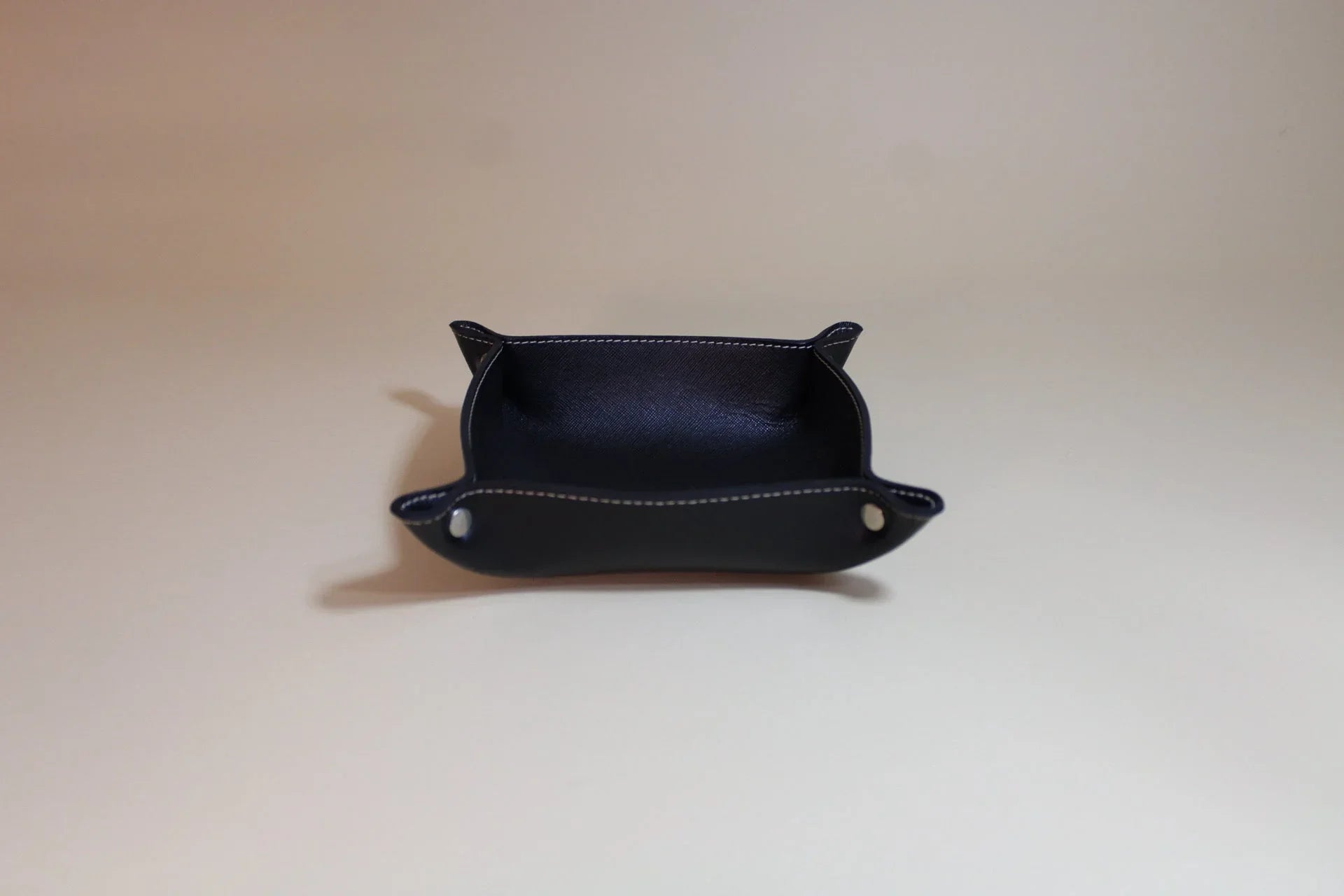 Black leather valet tray with white stitching on a neutral background