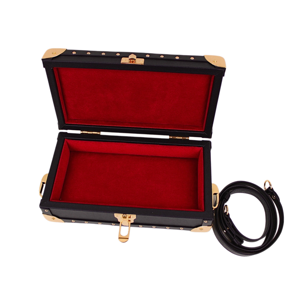 Open black jewelry box with red interior and gold accents, accompanied by a black cord on a white background.