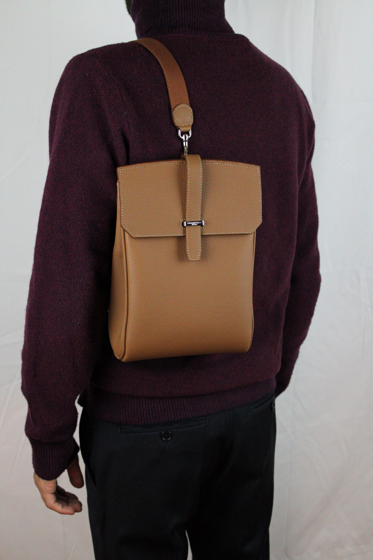Tan leather bag worn over a person's shoulder on a plain background