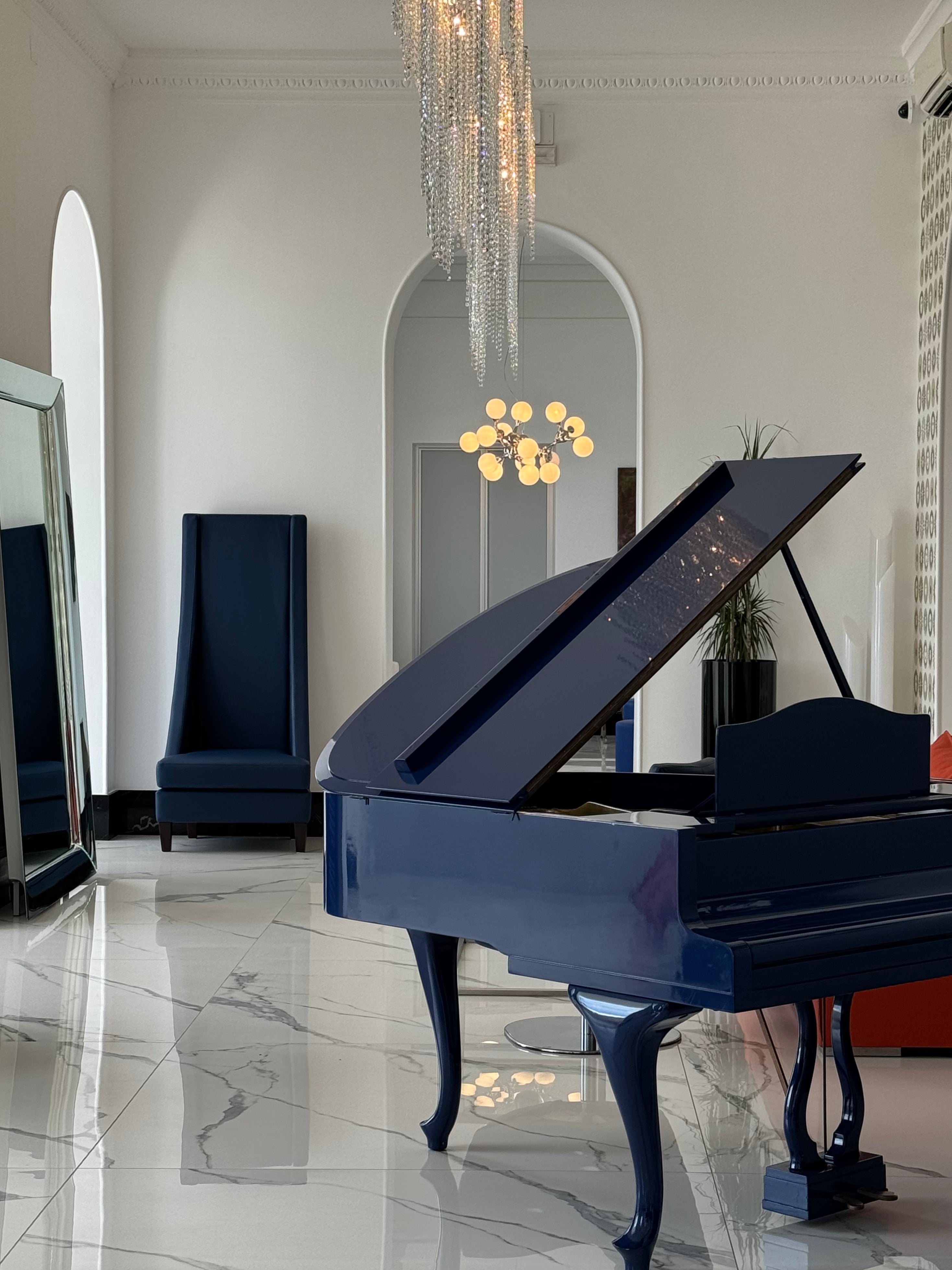 Blue grand piano in a stylish room with a chandelier and mirror.